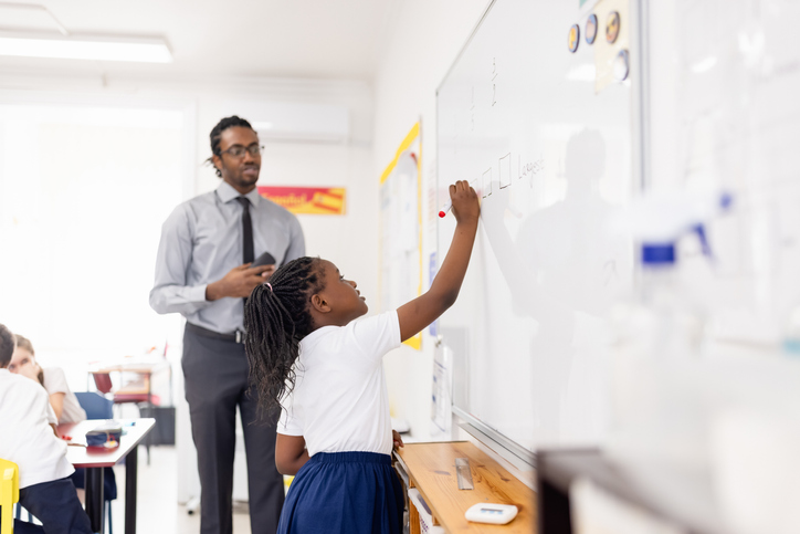 Primary school girl standing next to the white board, answering the question in the classroom.