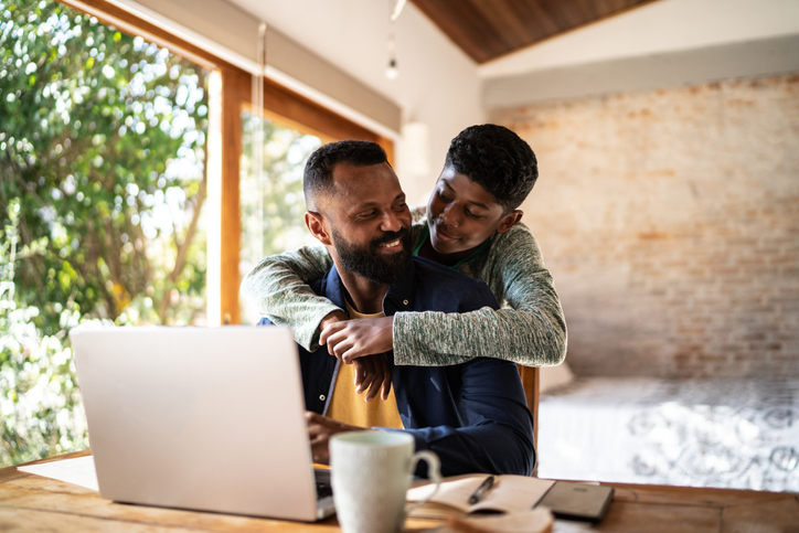 Son embracing father while he's working at home