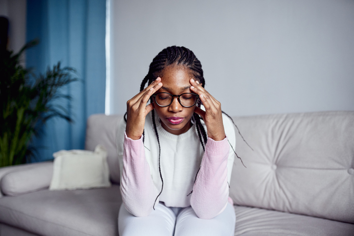 A young girl is sitting on the couch at home with her head in her hands.